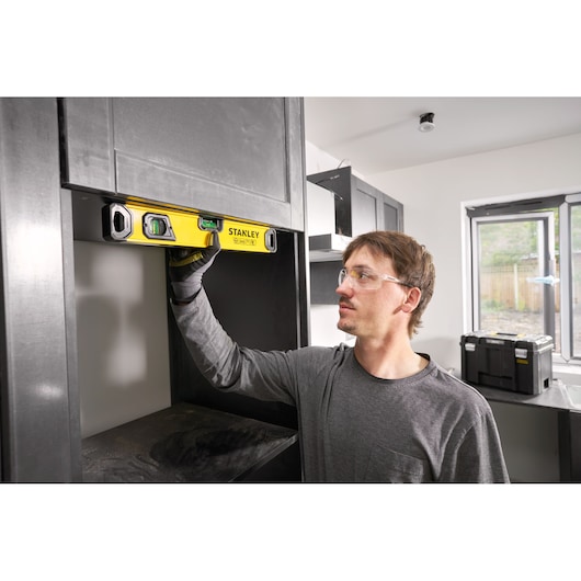 A person using a yellow STANLEY spirit level to check the alignment of a cabinet in a modern kitchen under construction.