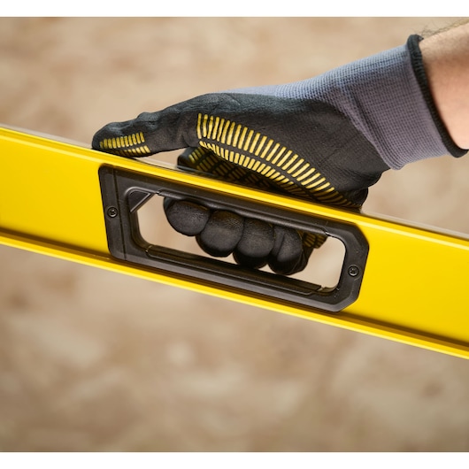 A close-up view of a gloved hand holding a yellow spirit level with a black handle.
