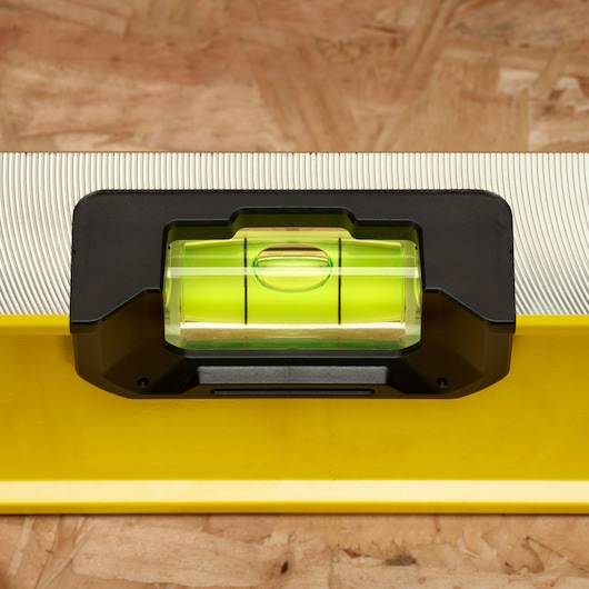 Close-up view of a Stanley spirit level tool with a yellow body and a green bubble vial, placed on a wooden surface.