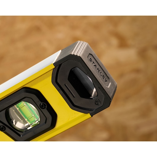Close-up of the end of a STANLEY yellow spirit level with a black and silver edge. The level features a green bubble vial and durable construction.