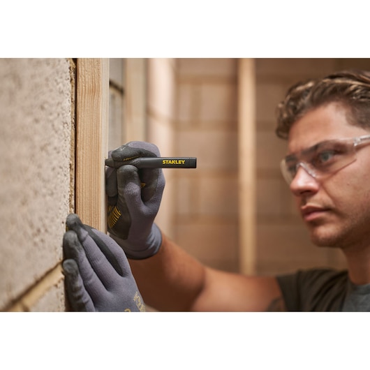 Person wearing gloves uses STANLEY marking pen to draw lines on wood during construction.