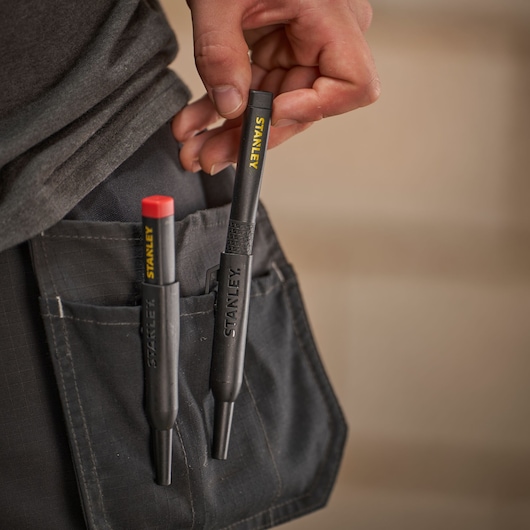 Two STANLEY marking tools in a work pocket, one being held by hand, designed for professional use.