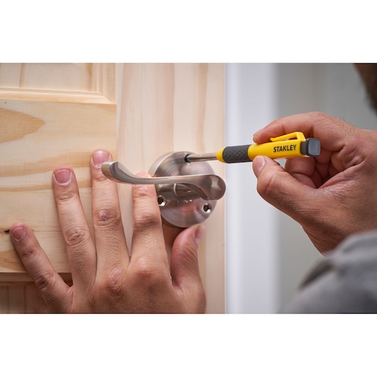 Person uses a Stanley screwdriver to tighten a screw on a metal door handle attached to a wooden door.