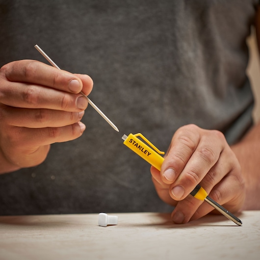 Hand holding a yellow Stanley voltage tester screwdriver, with another hand touching its metal tip.