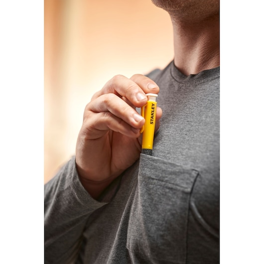 Person placing a yellow STANLEY tool in a gray shirt pocket, tool held upright with visible branding.