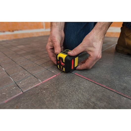 STANLEY STHT77502-1 laser level tool on floor tiles, projecting red alignment lines, close-up view.