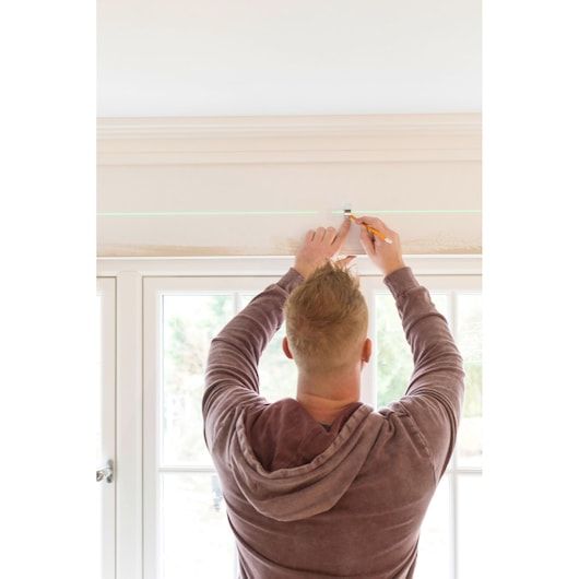 STANLEY STHT77592-1 laser level projecting green line on wall above window, person marking line, indoor use.