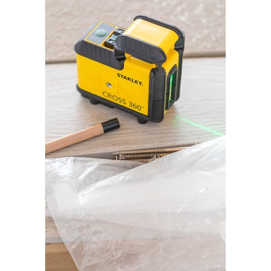 STANLEY STHT77594-1 laser level CROSS 360 on a wood surface with pencil, screws, and plastic sheet.