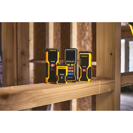 STANLEY STHT77666-0 laser distance measurers in yellow and black, on wooden beam, construction setting.