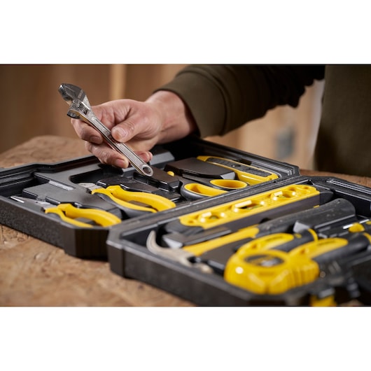 STANLEY STHT78050-1 tool set with yellow handles and a hand holding a wrench, in a black case.