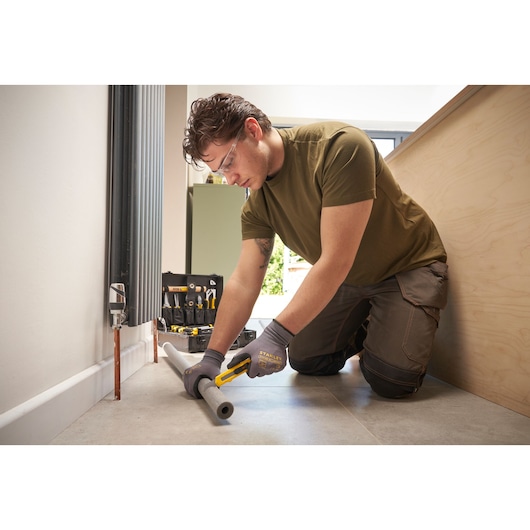 Photo of STANLEY STMT72986-1 tool kit in use, person cutting foam pipe insulation with utility knife on floor.
