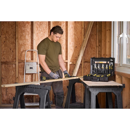 STANLEY STMT72986-1 tool kit open on workbench in workshop with worker measuring wood.