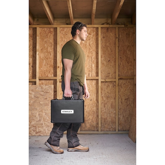 Stanley STMT72986-1 black tool case held by person, indoor workshop setting, product side view.