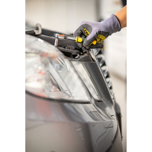 STANLEY STMT82663-0 ratchet wrench used on car headlight, close-up with gloved hand.