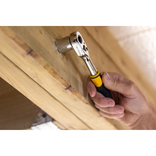 STANLEY STMT82670-0 ratchet wrench with yellow-black handle in use on wooden surface, close-up.
