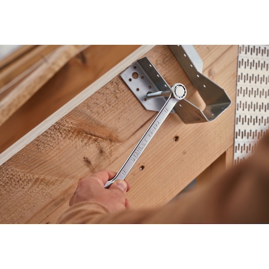 Photo of STANLEY STMT82843-0 combination wrench in use tightening a bolt on a metal bracket and wooden frame.