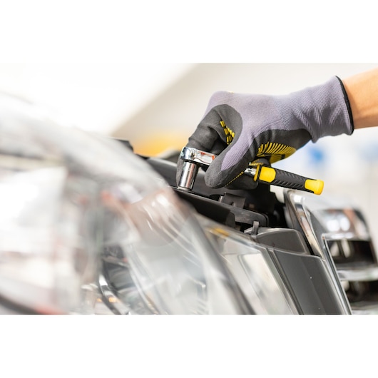 STANLEY STMT86111-0 ratchet wrench being used on a car headlight by a gloved hand, close-up photo.