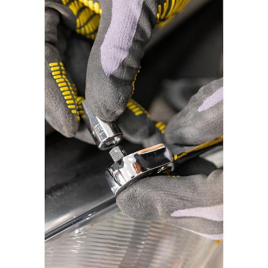 STANLEY STMT86112-0 photography of gloved hands using a chrome ratchet and socket tool on machinery.