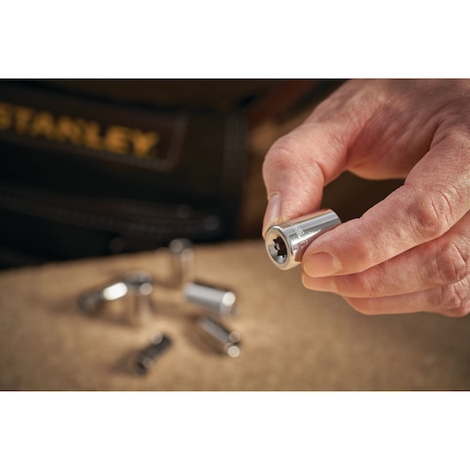 STANLEY STMT86114-0 socket held in hand with other sockets blurred on a workbench, photography product image.