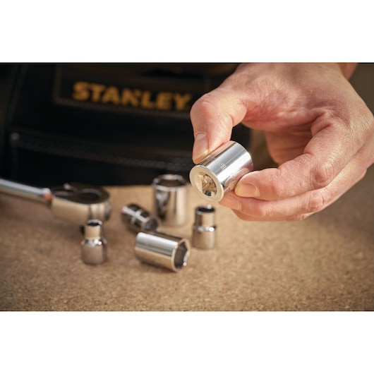 STANLEY STMT86314-0 chrome socket set, close-up of hand holding socket with additional sockets on table.