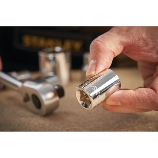 STANLEY STMT86532-0 chrome socket held by hand, ratchet wrench and sockets in background, close-up.