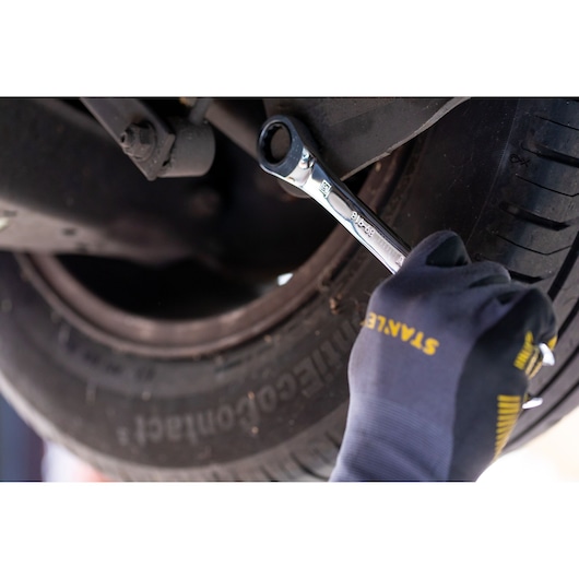 STANLEY STMT89908-0 ratcheting wrench used on car wheel bolt, close-up with gloved hand.