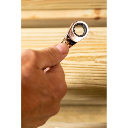 STANLEY STMT89909-0 ratcheting wrench held in hand against wooden boards, close-up photography.