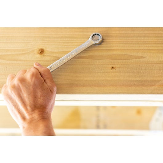 Photo of STANLEY STMT95792-0 ratcheting wrench in hand tightening bolt on wooden surface.