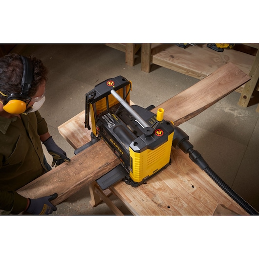 Photo of STANLEY STP18-B2 planer in use, smoothing a wooden board in a workshop from a top angle.