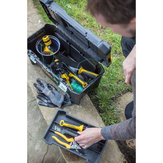 STANLEY STST1-75521 tool box with open lid, showing garden tools and gloves, top-down outdoor view.