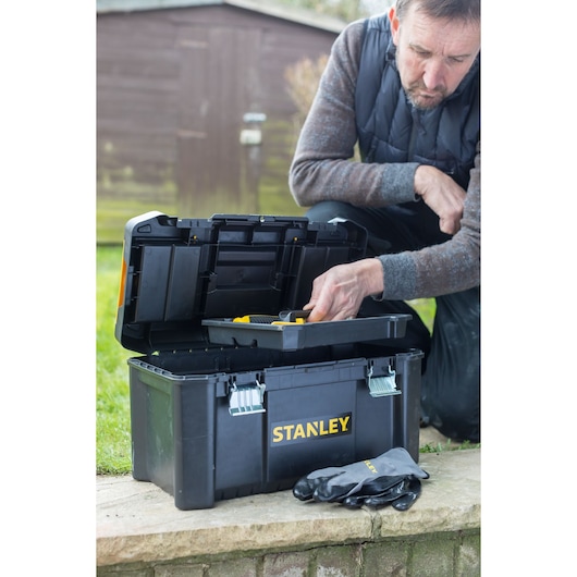 Photo of STANLEY STST1-75521 toolbox outdoors, lid open showing tray, gloves placed in front, person using it.