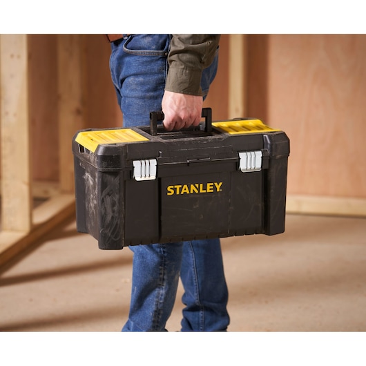 Stanley STST1-75521 black and yellow toolbox held by person, shown in workshop setting.