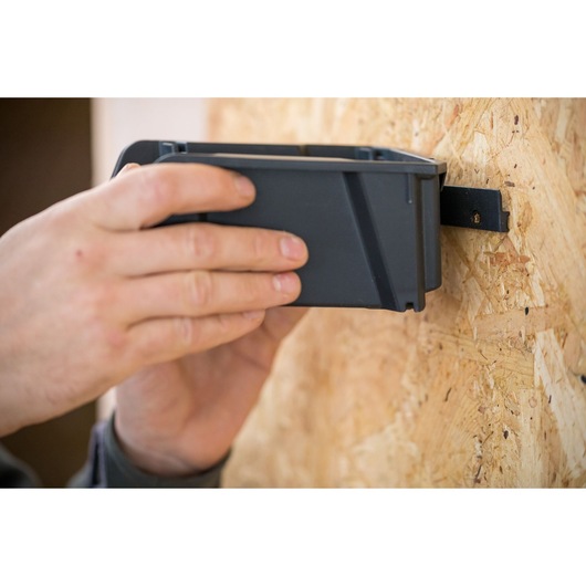 STANLEY STST82733-1 storage bin being mounted on wood wall, close-up of hands and bin.