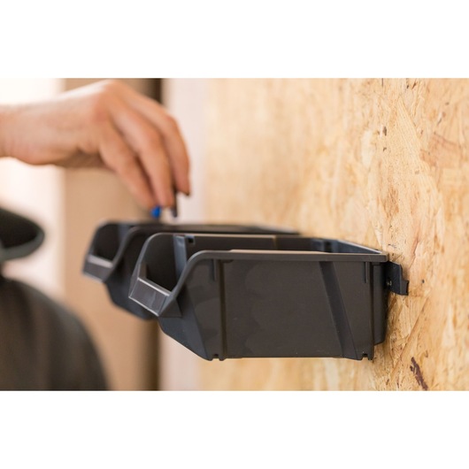 STANLEY STST82733-1 black wall-mounted storage bins, side angle, hand placing tool in bin.