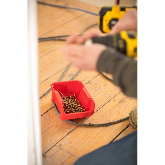 STANLEY STST82736-1 red storage bin holding screws on wooden floor, angled view, tradesperson working nearby.