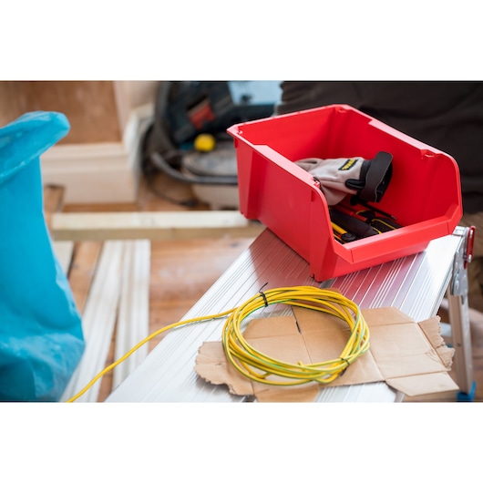 STANLEY STST82742-1 red storage bin with gloves and tools, photographed on a silver workbench with yellow wire.