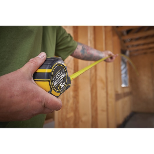Photo of STANLEY XTHT0-33671 tape measure, black and yellow, being used in a wooden construction interior.